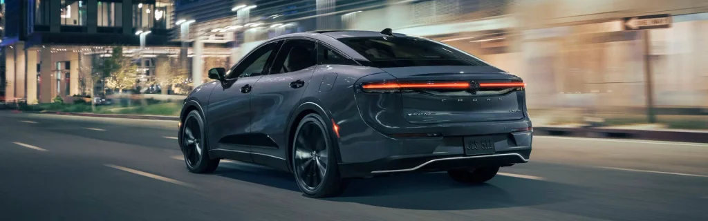 The image shows a Toyota Crown sedan driving through a city street at night.