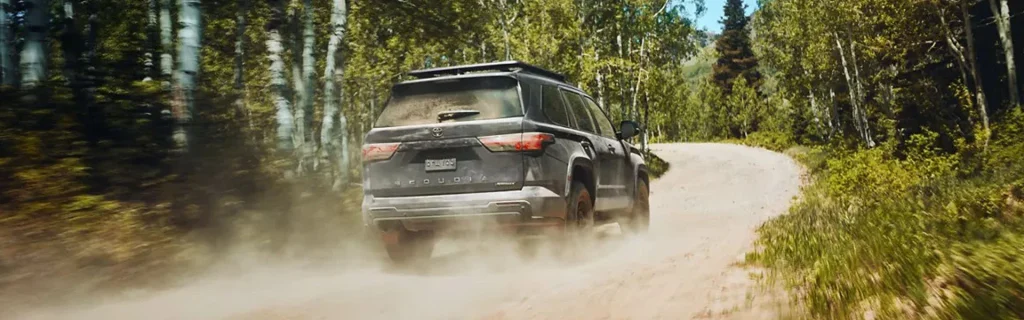 The image shows a Toyota Sequoia driving off-road on a dirt trail through a forested area.