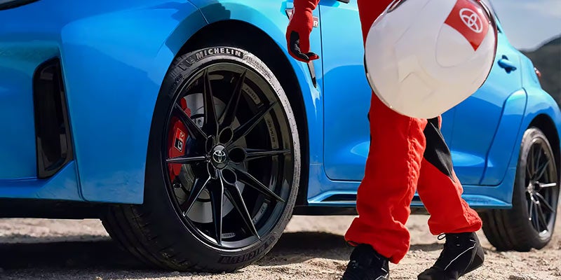 Image of a racecar driver next to a blue Toyota GR Corolla