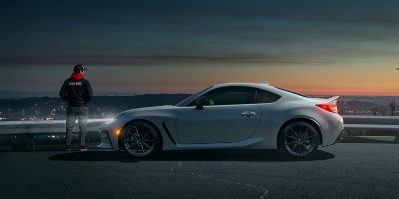 Image of a white Toyota GR86 driving parked with the driver by the front end
