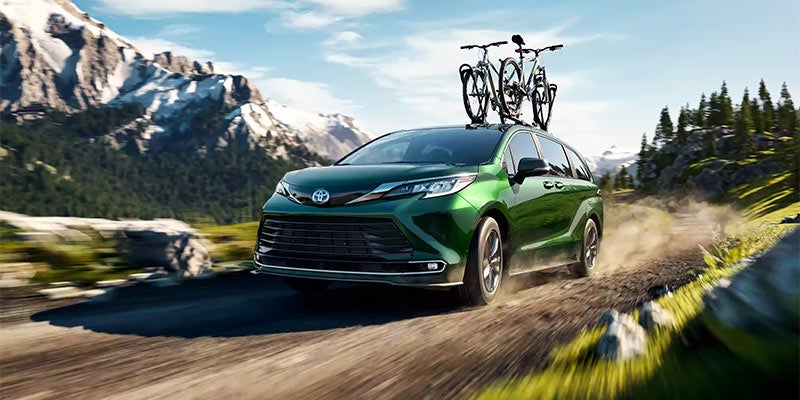 Image of a 2024 Toyota Sienna driving in the mountains with 2 bikes strapped to the top of the car