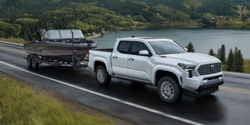 A white 2024 Toyota Tacoma pulling a Trailor thru a mountain road